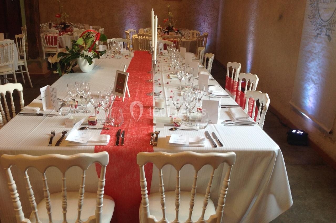 Table de réception élégamment dressée avec nappes blanches, chemin de table rouge et chaises en bois blanc.