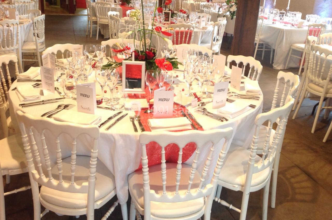 Table ronde décorée pour un événement, avec nappes blanches, chaises assorties, verres, menus et centre de table floral.