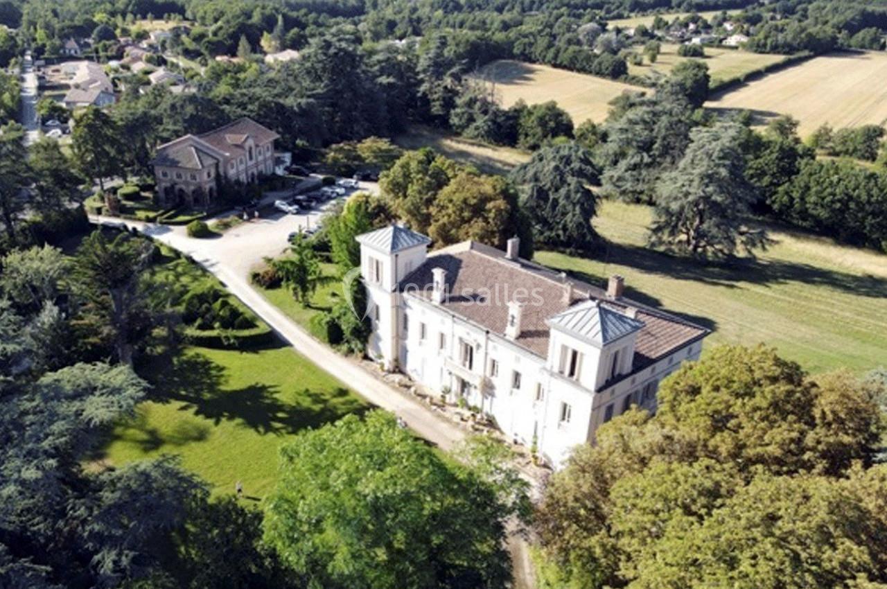 Vue aérienne d'un château entouré de jardins verdoyants et de champs, avec des bâtiments annexes à proximité.