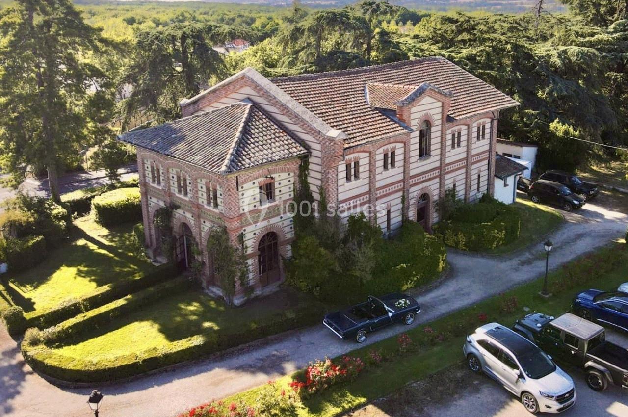 Vue aérienne d'un bâtiment en briques entouré de verdure, avec des voitures garées à proximité.