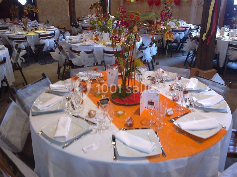 Table ronde décorée pour un événement, avec nappes blanches, chemin de table orange, verres et couverts élégants.