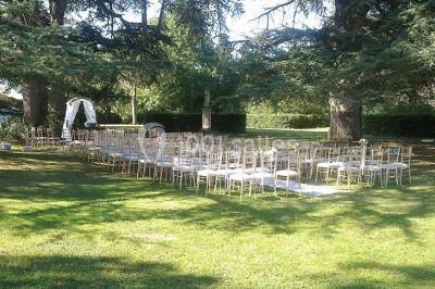 Intérieur d'une tente de réception avec tables rondes décorées, chaises en bois clair et lumière naturelle.