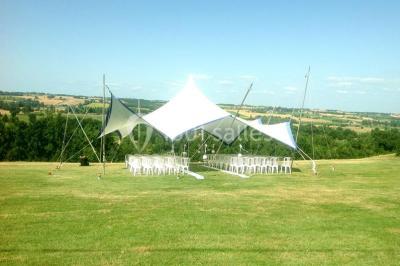 Intérieur d'une tente de réception avec tables rondes décorées, chaises en bois clair et lumière naturelle.