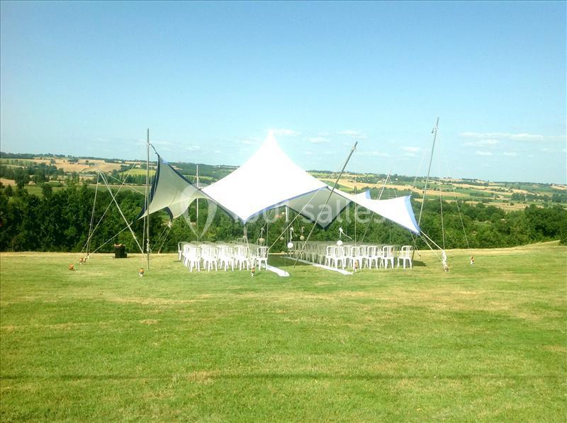 Tente blanche montée sur une pelouse, entourée de chaises blanches, avec une vue dégagée sur la campagne.