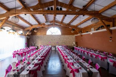 Salle de réception décorée pour un mariage, avec des tables alignées et nappes blanches ornées de nœuds roses.