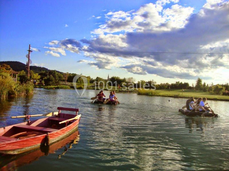 Des personnes naviguent sur des radeaux sur un lac entouré de végétation, avec un ciel partiellement nuageux.