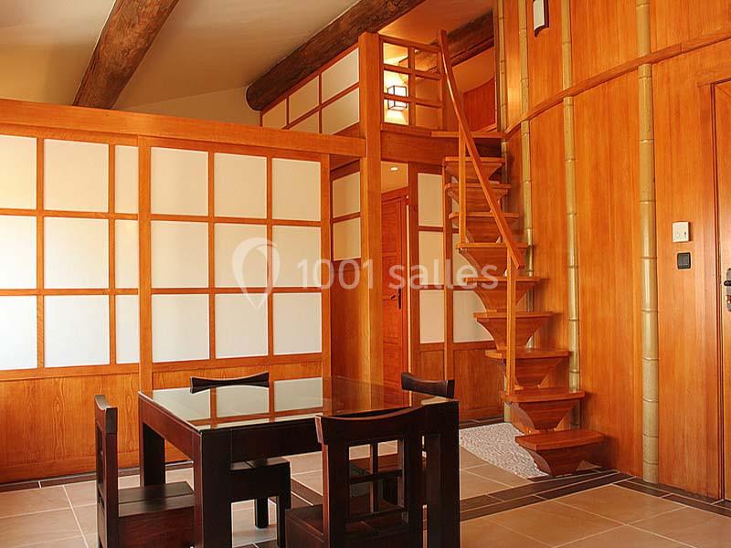 Salle à manger de style japonais avec table en bois, chaises assorties et escalier menant à une mezzanine.