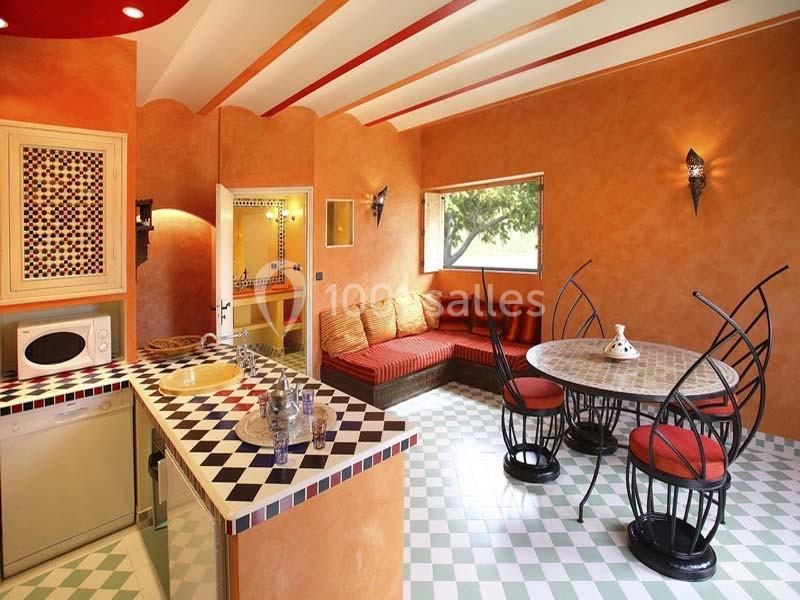 Cuisine lumineuse au style méditerranéen avec murs orange, carreaux colorés, table ronde et banquette près d'une fenêtre.