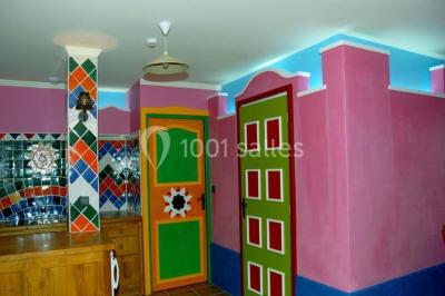 Salle de réception décorée pour un mariage, avec des tables alignées et nappes blanches ornées de nœuds roses.