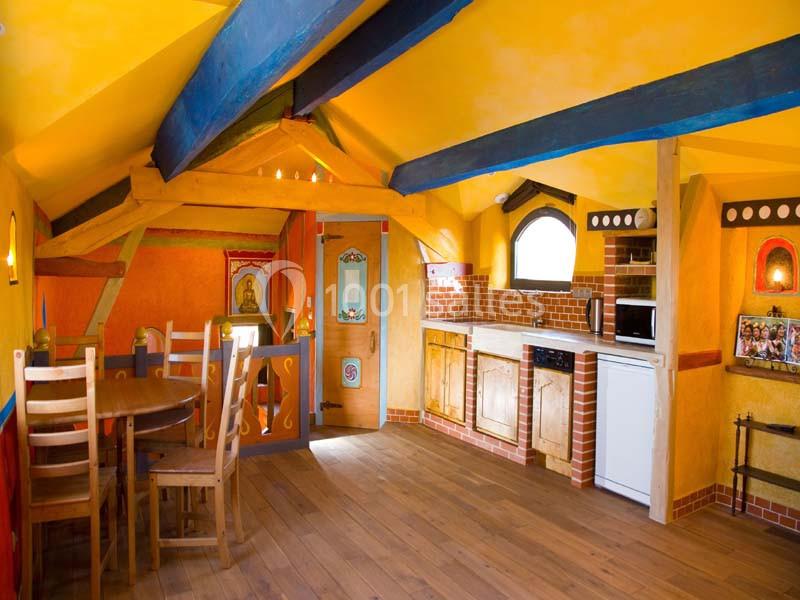 Cuisine ouverte colorée avec poutres apparentes, coin repas en bois, meubles rustiques et lumière naturelle.