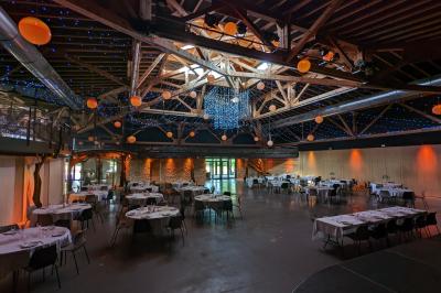 Salle de réception décorée pour un mariage, avec des tables alignées et nappes blanches ornées de nœuds roses.