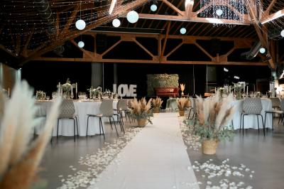 Salle de réception décorée pour un mariage, avec des tables alignées et nappes blanches ornées de nœuds roses.