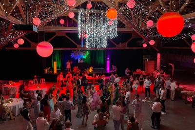 Salle de réception décorée pour un mariage, avec des tables alignées et nappes blanches ornées de nœuds roses.