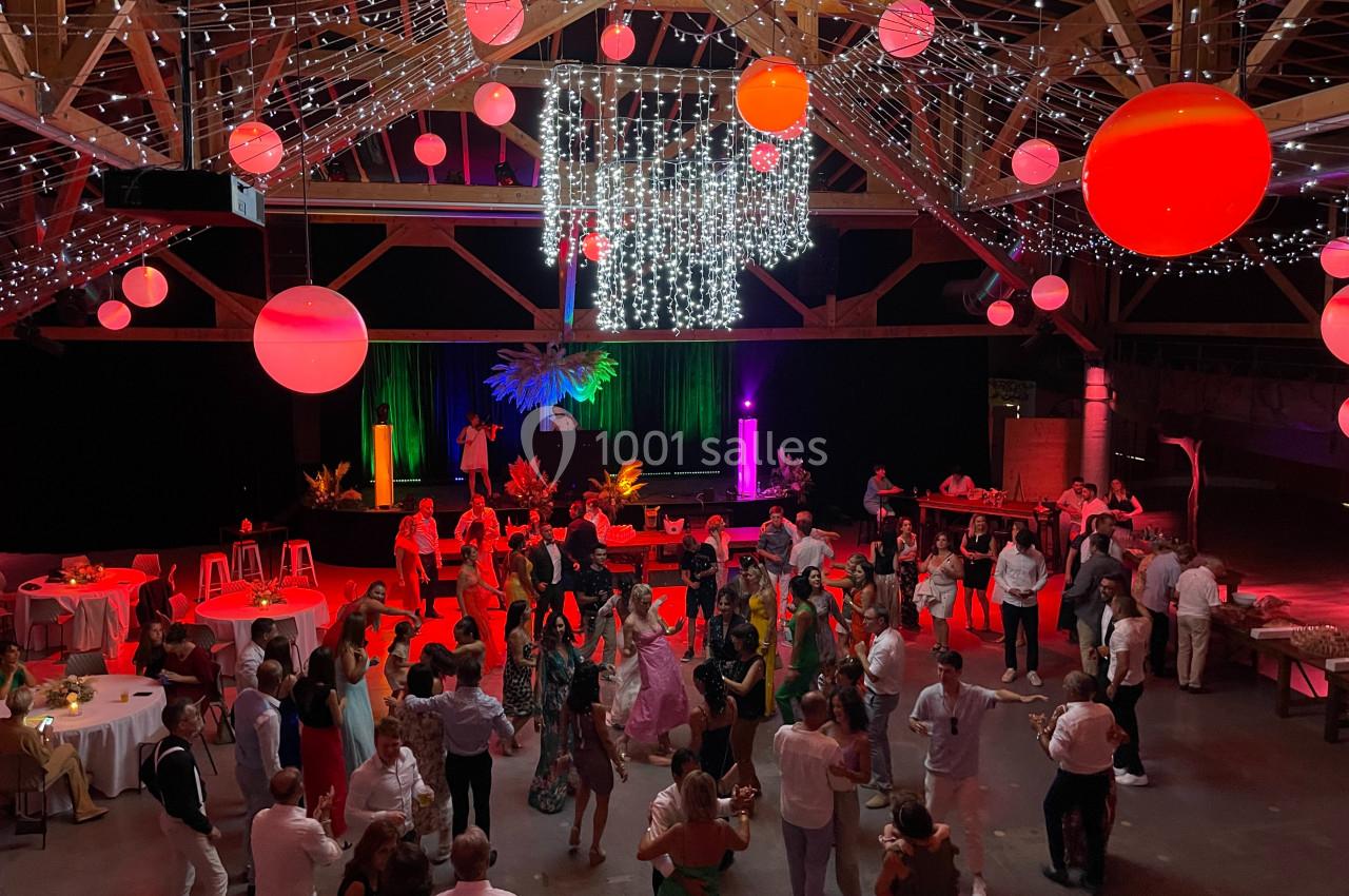 Salle festive avec des invités dansant sous des lumières colorées, des décorations suspendues et des tables disposées autour.