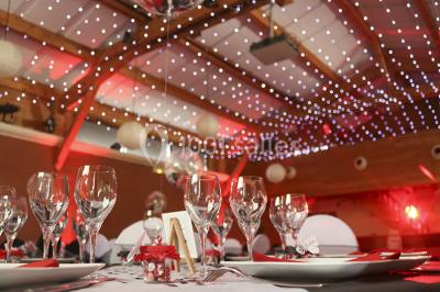 Salle de réception décorée pour un mariage, avec des tables alignées et nappes blanches ornées de nœuds roses.