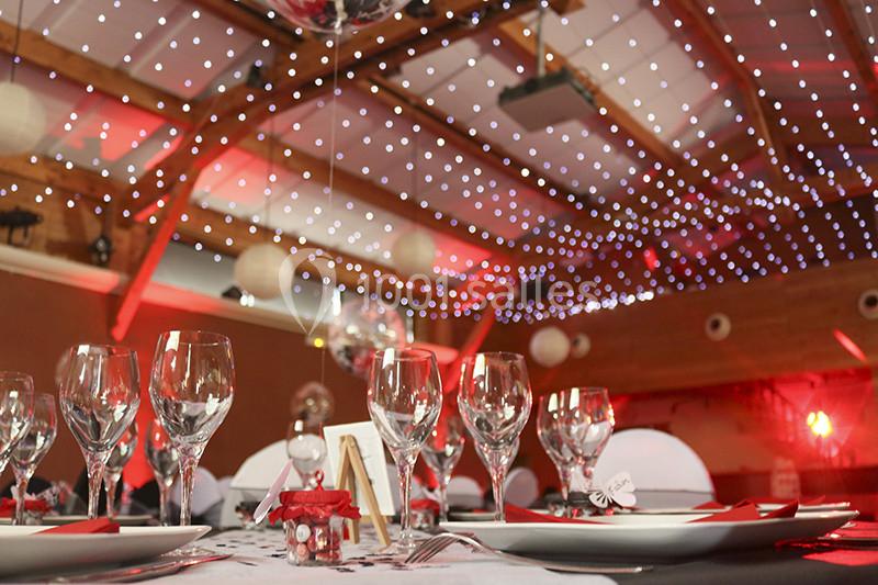 Salle de réception décorée avec des guirlandes lumineuses au plafond, tables dressées avec verres et décorations.