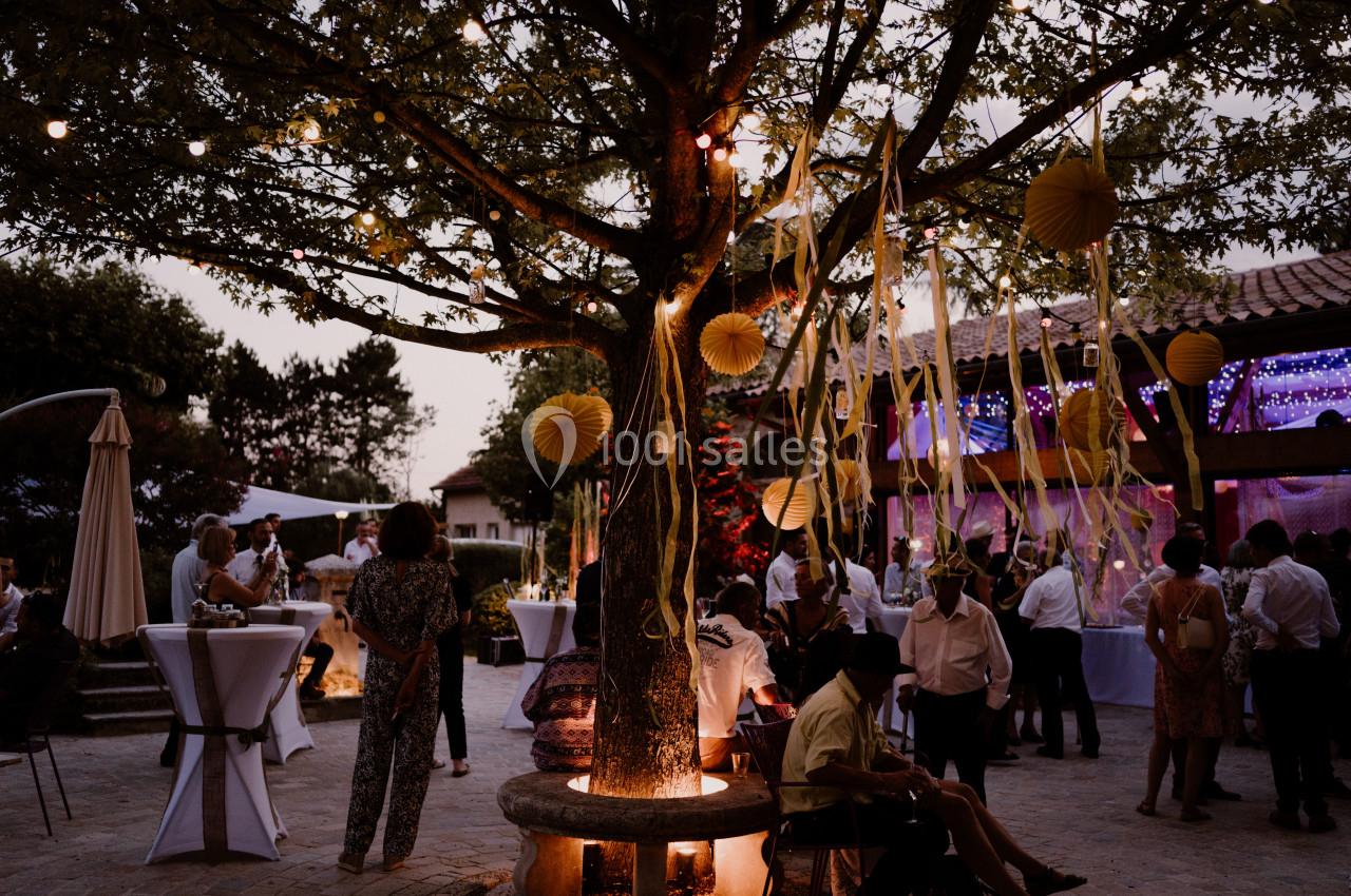 Un arbre décoré de guirlandes lumineuses et de lanternes jaunes au centre d'une fête en plein air au crépuscule.