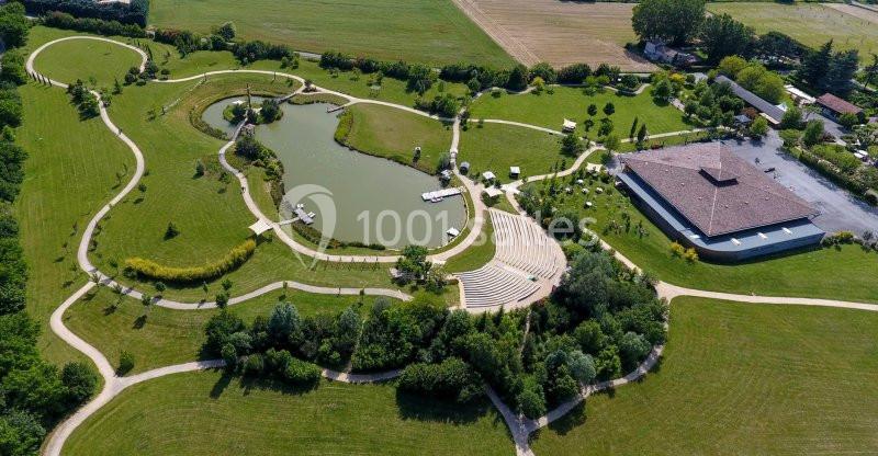 Vue aérienne d'un parc avec un étang, des allées sinueuses, un amphithéâtre en plein air et un bâtiment entouré de verdure.