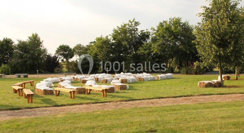 Bottes de paille recouvertes de tissu blanc disposées en sièges dans un espace extérieur herbeux avec des bancs en bois.