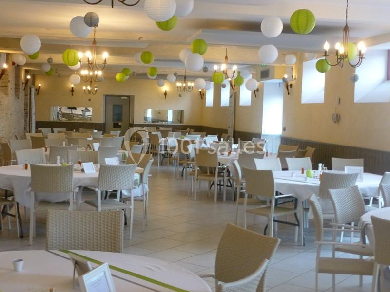 Salle de réception décorée de lanternes blanches et vertes, avec des tables rondes dressées et des chaises en osier clair.