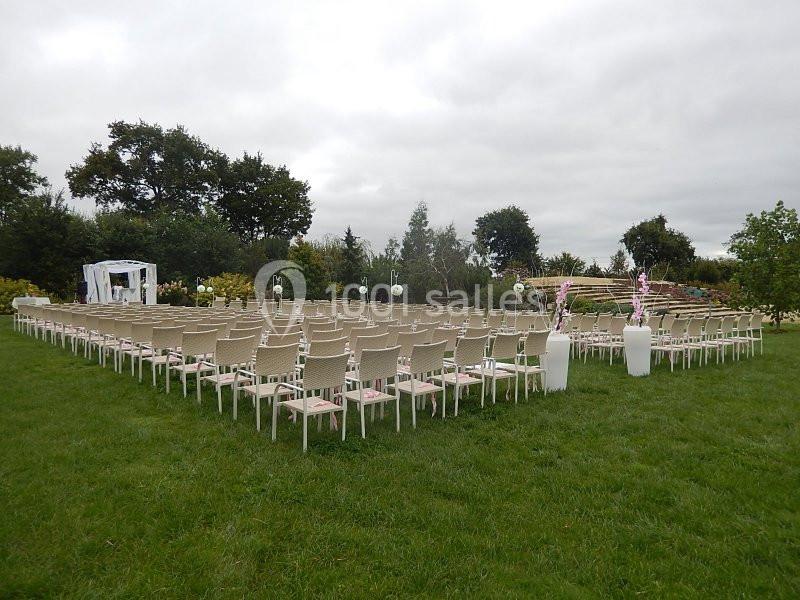 Chaises disposées en carré sur une pelouse, face à une arche décorée, dans un cadre extérieur verdoyant.