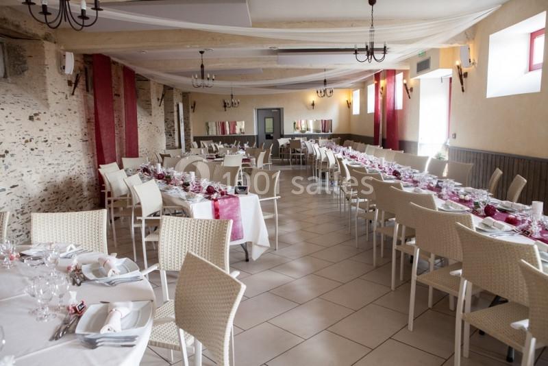 Salle de réception décorée avec des tables dressées, nappes blanches et touches de rouge, éclairée par la lumière naturelle.