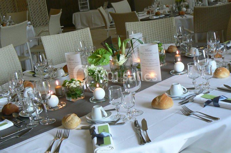 Table élégamment dressée avec nappes blanches, couverts, verres, bougies, menus et décorations florales.