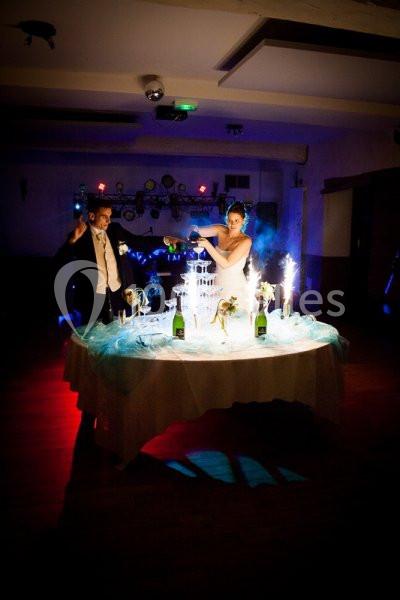 Un couple habillé en tenue de mariage verse du champagne dans une fontaine illuminée sur une table décorée.