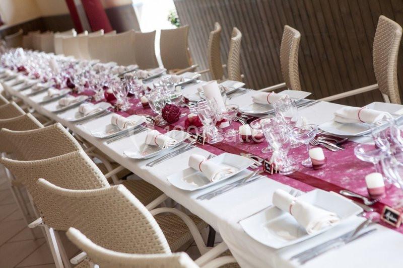 Table dressée pour un repas, avec nappe blanche, chemin de table rouge, vaisselle et verres alignés.