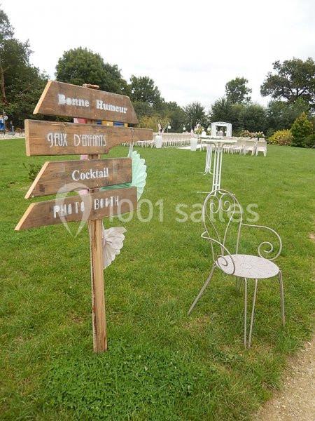 Panneau en bois indiquant différentes directions lors d'un événement en plein air, avec une chaise et des tables en arrière…
