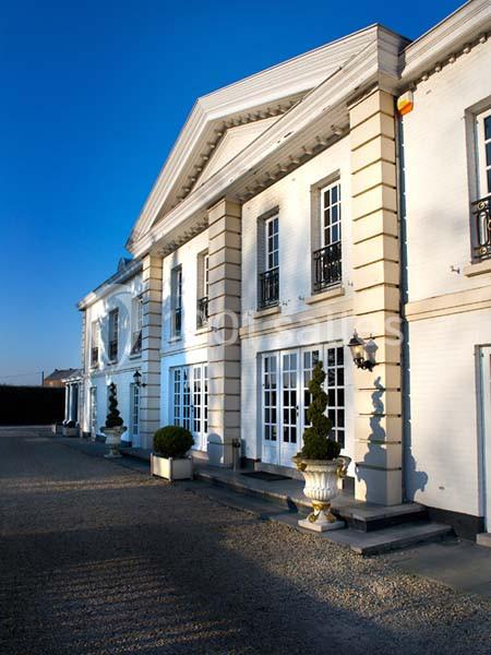 Façade d'un grand bâtiment blanc de style classique avec colonnes et fenêtres, entouré de pots décoratifs.