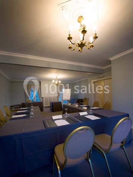 Salle de réunion avec table rectangulaire, chaises, paperboard, blocs-notes et éclairage par lustres.