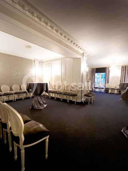 Salle élégante avec des murs ornés, des chaises alignées le long des murs et une table haute drapée au centre.
