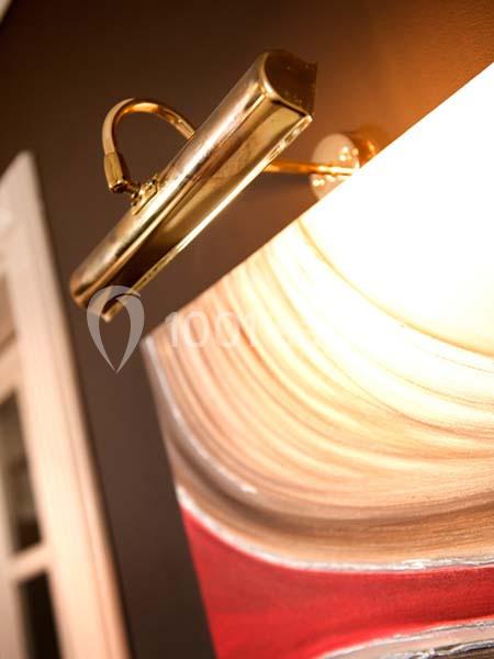 Lampe dorée éclairant un tableau abstrait aux teintes rouges et beiges sur un mur sombre.