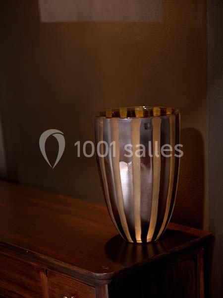 Vase décoratif rayé en verre, posé sur un meuble en bois sombre dans un intérieur faiblement éclairé.