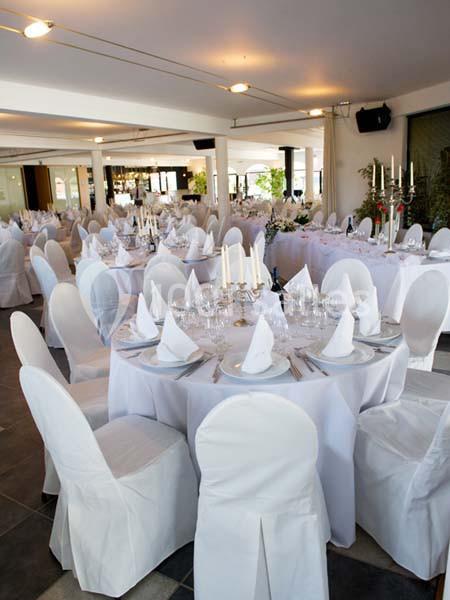 Salle de réception décorée avec des tables rondes dressées, nappes blanches et chandeliers.