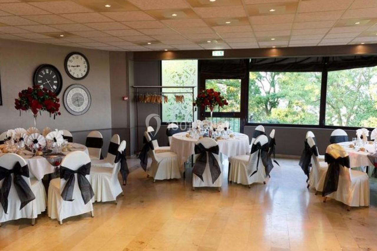 Salle de réception décorée avec des tables rondes dressées, chaises ornées de nœuds noirs et grandes fenêtres donnant sur un…