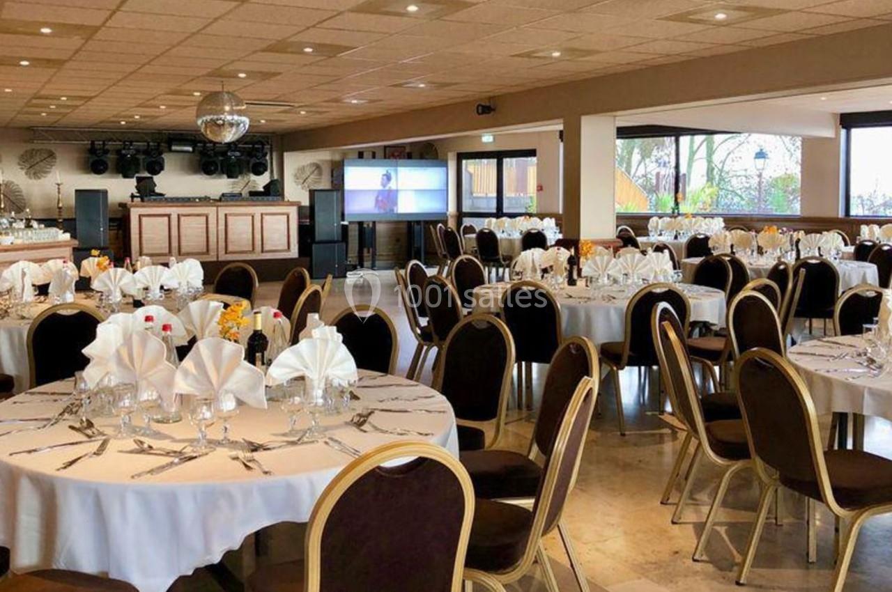 Salle de réception avec tables rondes dressées, nappes blanches, serviettes pliées et décoration élégante.