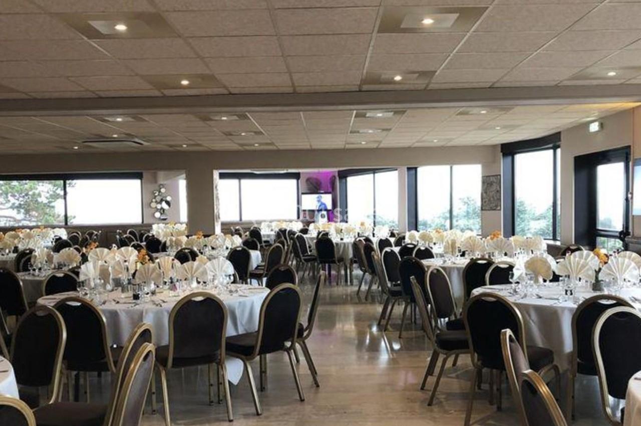 Salle de réception lumineuse avec des tables rondes dressées pour un événement, décorées de nappes blanches et serviettes…