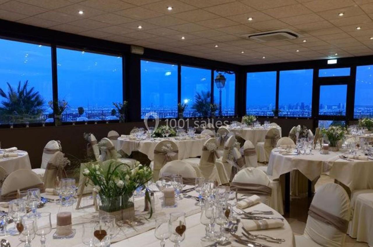 Salle de réception élégamment décorée avec des tables rondes dressées, offrant une vue panoramique sur un paysage urbain.