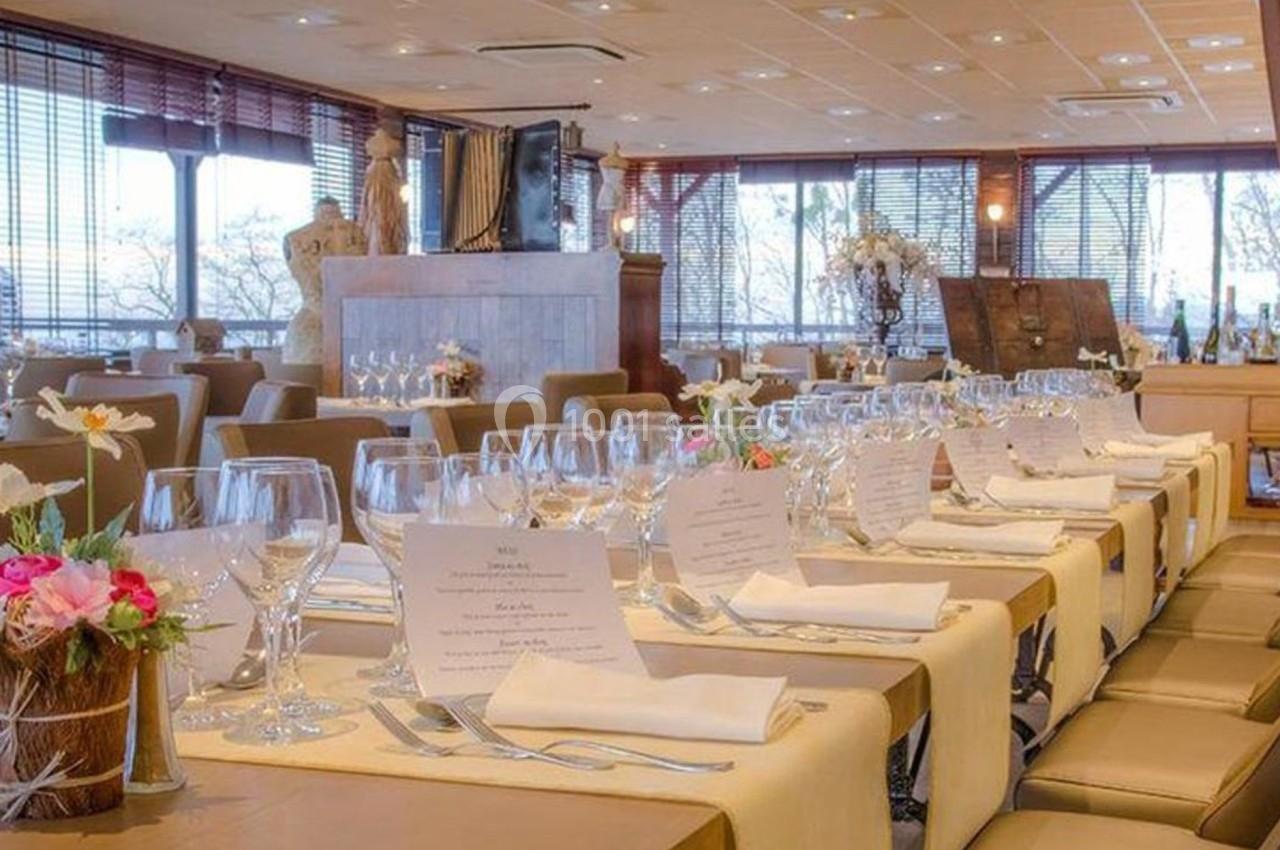 Salle de restaurant élégante avec tables dressées, nappes beige, verres, menus et décorations florales.