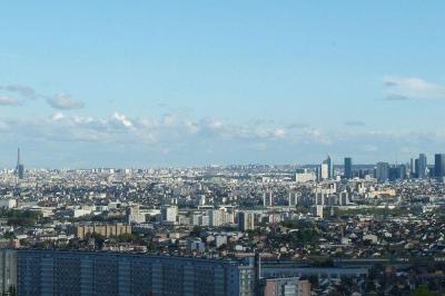 Vue panoramique d'une ville avec la tour Eiffel à gauche et des gratte-ciels modernes à droite sous un ciel dégagé.