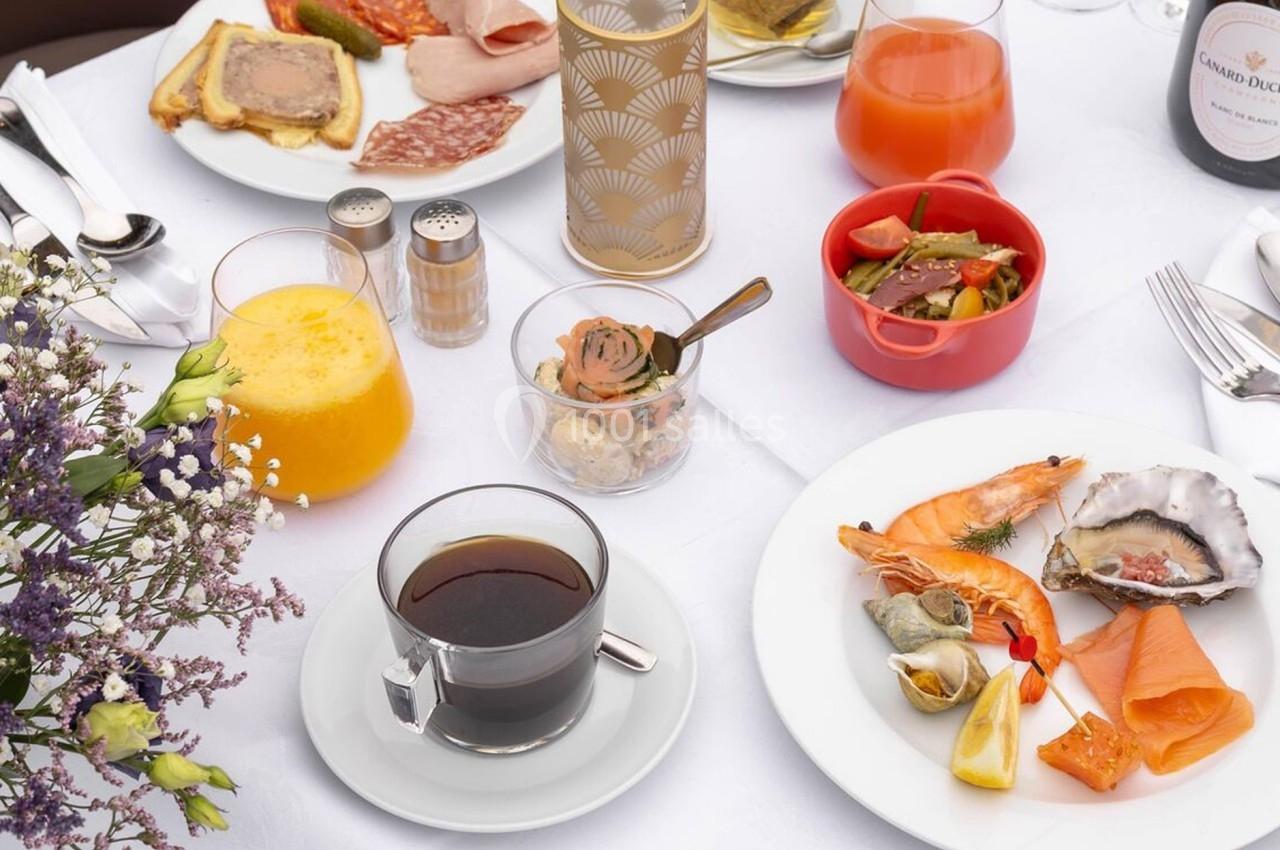 Table dressée avec un assortiment de mets : fruits de mer, charcuterie, jus, café, fleurs et condiments.