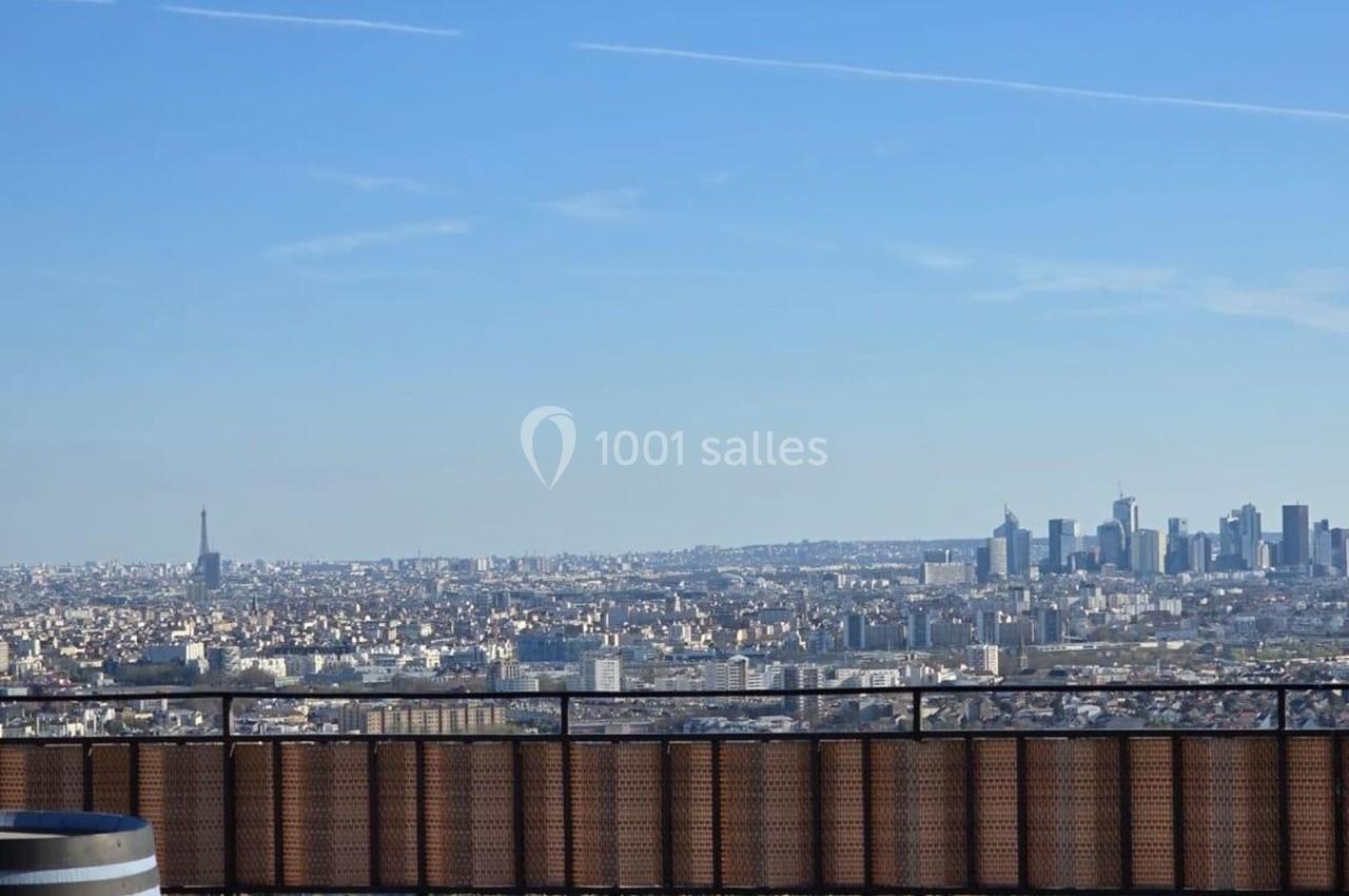 Vue panoramique sur Paris avec la tour Eiffel à gauche et les gratte-ciel de La Défense à droite, sous un ciel dégagé.