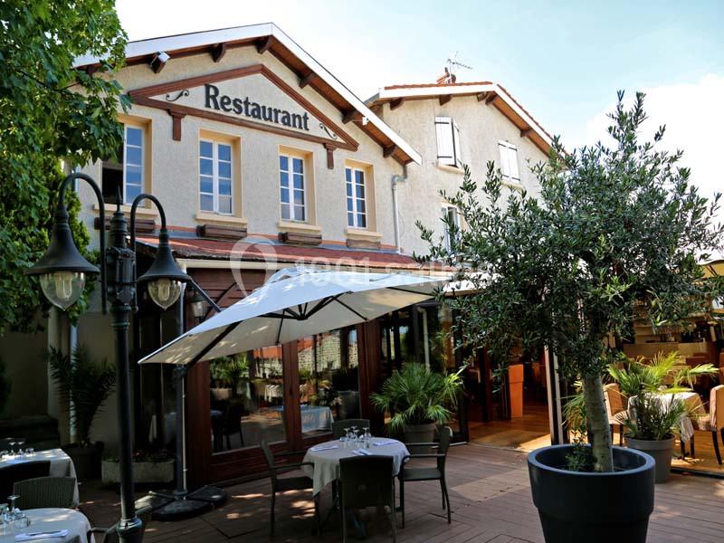 Façade d'un restaurant avec terrasse aménagée, tables dressées, parasols et végétation environnante.