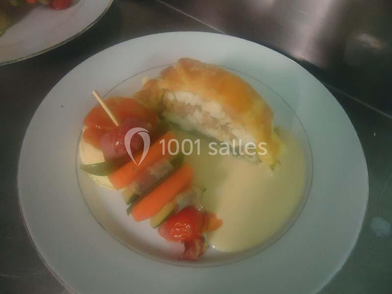 Plat composé d'un feuilleté farci, d'une brochette de légumes et d'une sauce crémeuse, servi sur une assiette blanche.