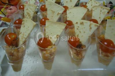 Menu posé sur une table dressée en extérieur, entourée de verres, fleurs et paysage verdoyant en arrière-plan.