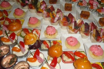 Menu posé sur une table dressée en extérieur, entourée de verres, fleurs et paysage verdoyant en arrière-plan.