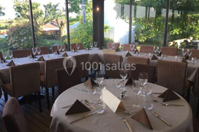 Menu posé sur une table dressée en extérieur, entourée de verres, fleurs et paysage verdoyant en arrière-plan.