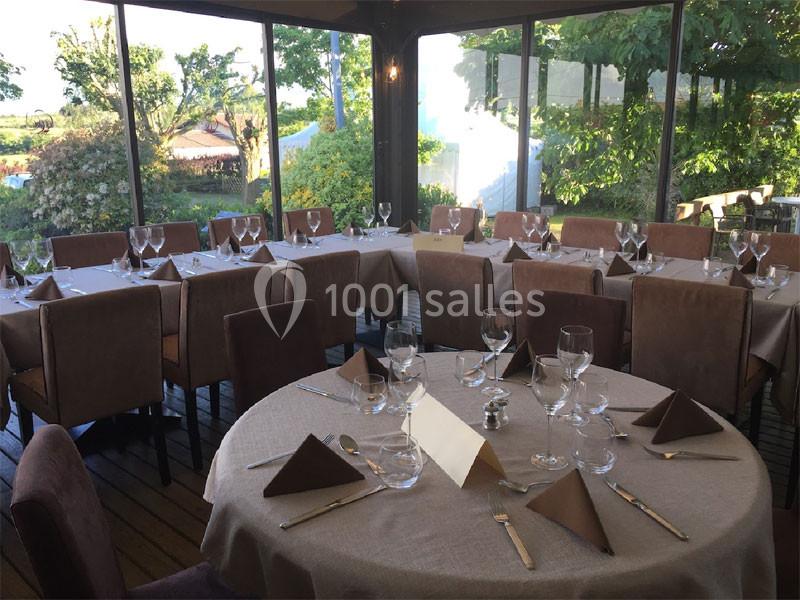 Salle de restaurant lumineuse avec tables dressées, nappes beige, serviettes pliées et vue sur un jardin verdoyant.